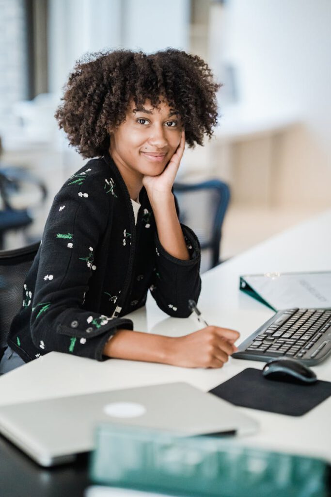 A woman with curly hair smiles while working at a desk in a bright office setting.