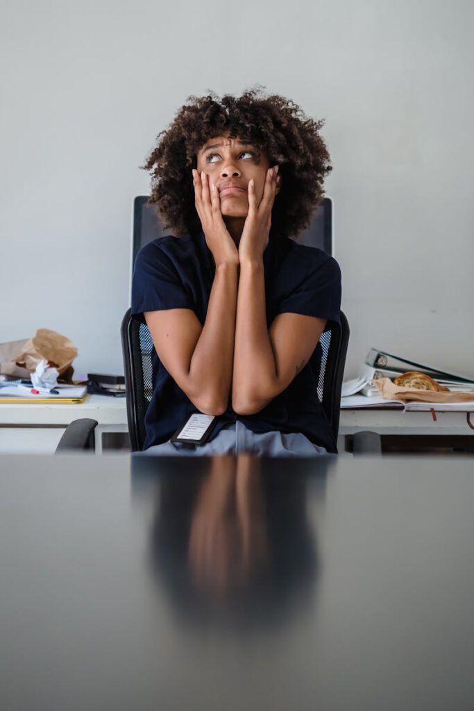 Contemplative woman in office, hands on face, expressing frustration.